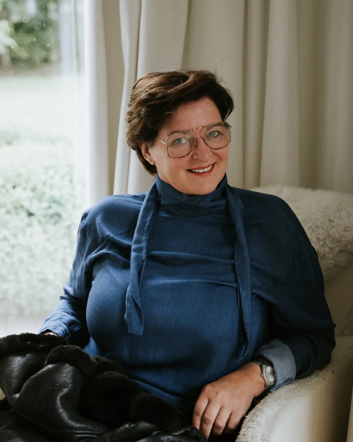 Woman wearing a blue sweater sitting on a couch with a window in the background